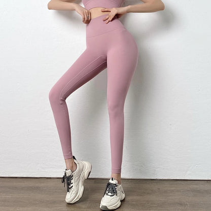 Person wearing pink leggings and white sneakers against a white wall.