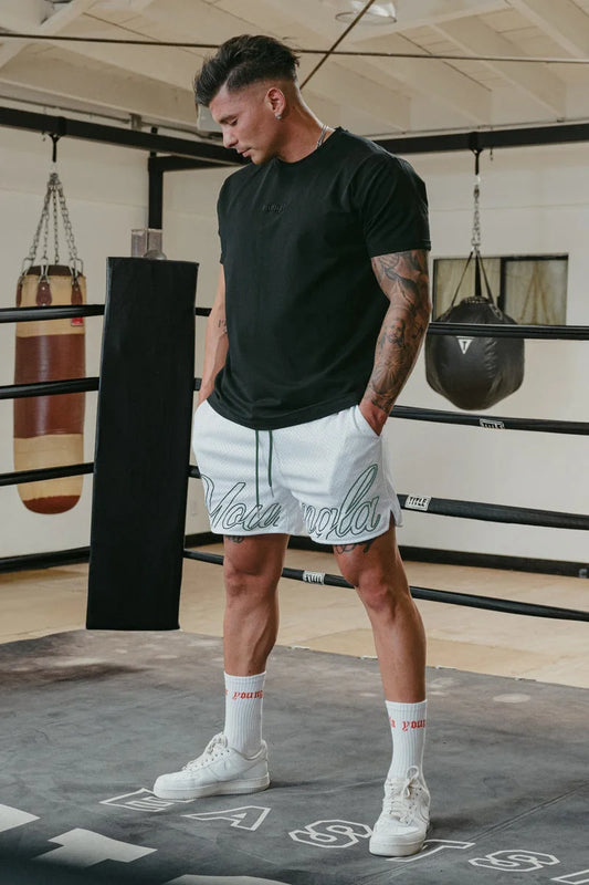 Man in black t-shirt and white shorts standing in a boxing ring.