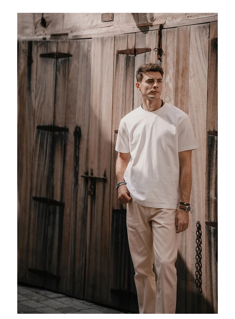 Man wearing a white t-shirt and beige pants standing in front of wooden doors.