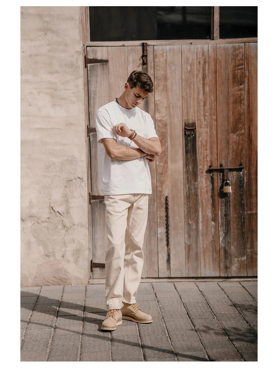 Man in a white t-shirt and beige pants standing in front of a wooden door.