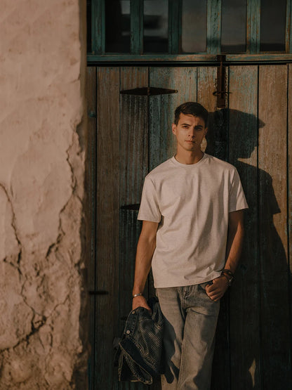 Man in a white t-shirt and jeans standing against a rustic wooden door.