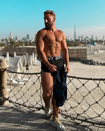 Man posing shirtless on a rooftop with a city skyline in the background