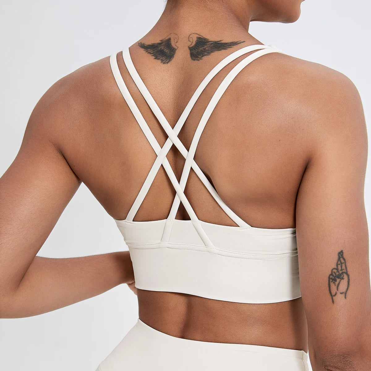 Person wearing a white sports bra with criss-cross straps on a plain background
